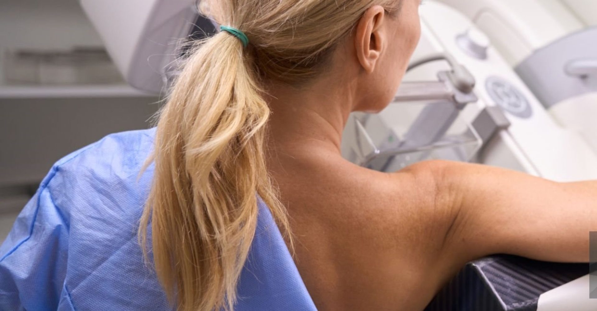 Back view of Caucasian female patient undergoing 3D mammography in radiology room