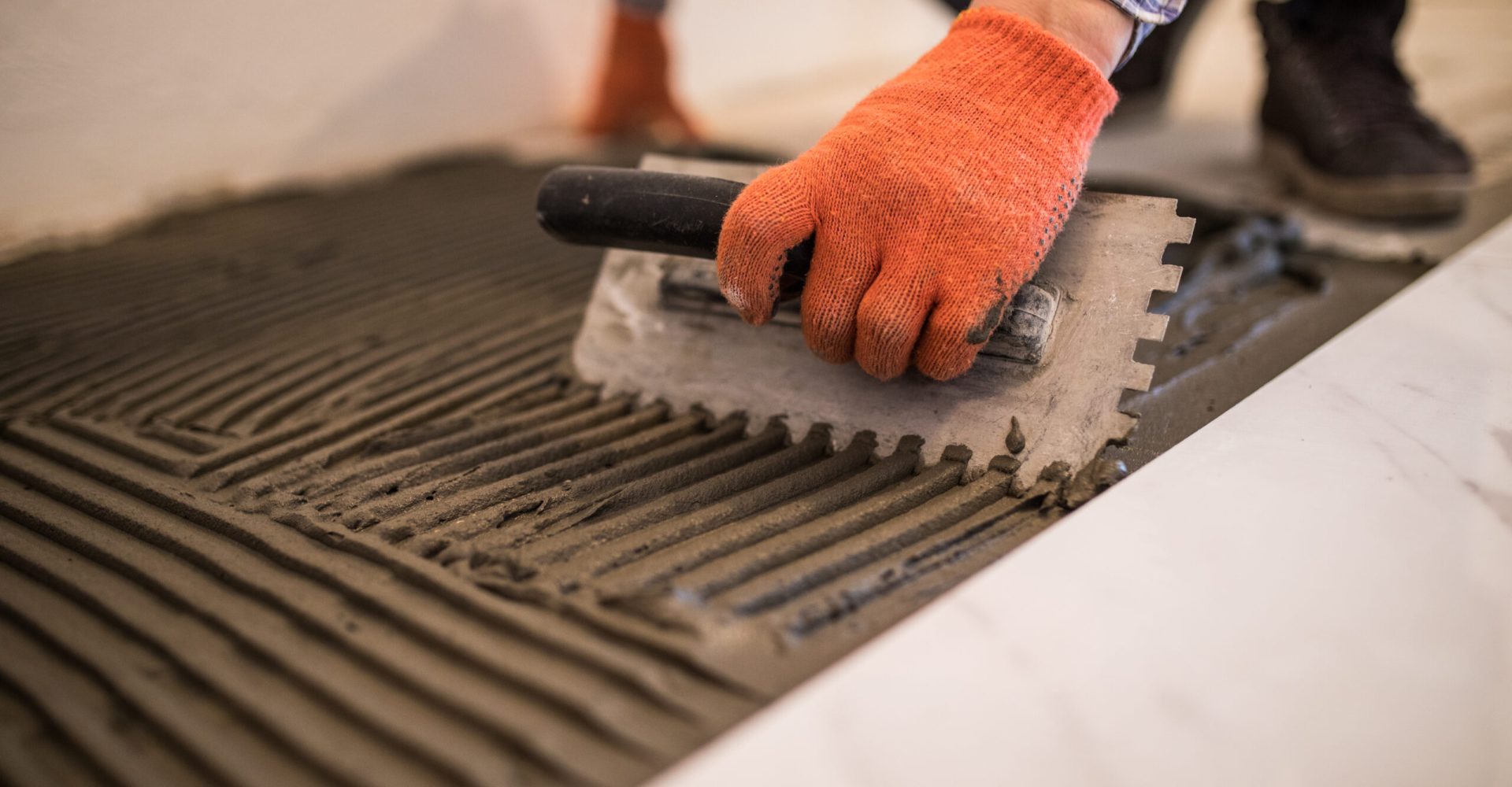 Laying Ceramic Tiles. Troweling mortar onto a concrete floor in preparation for laying white floor tile.