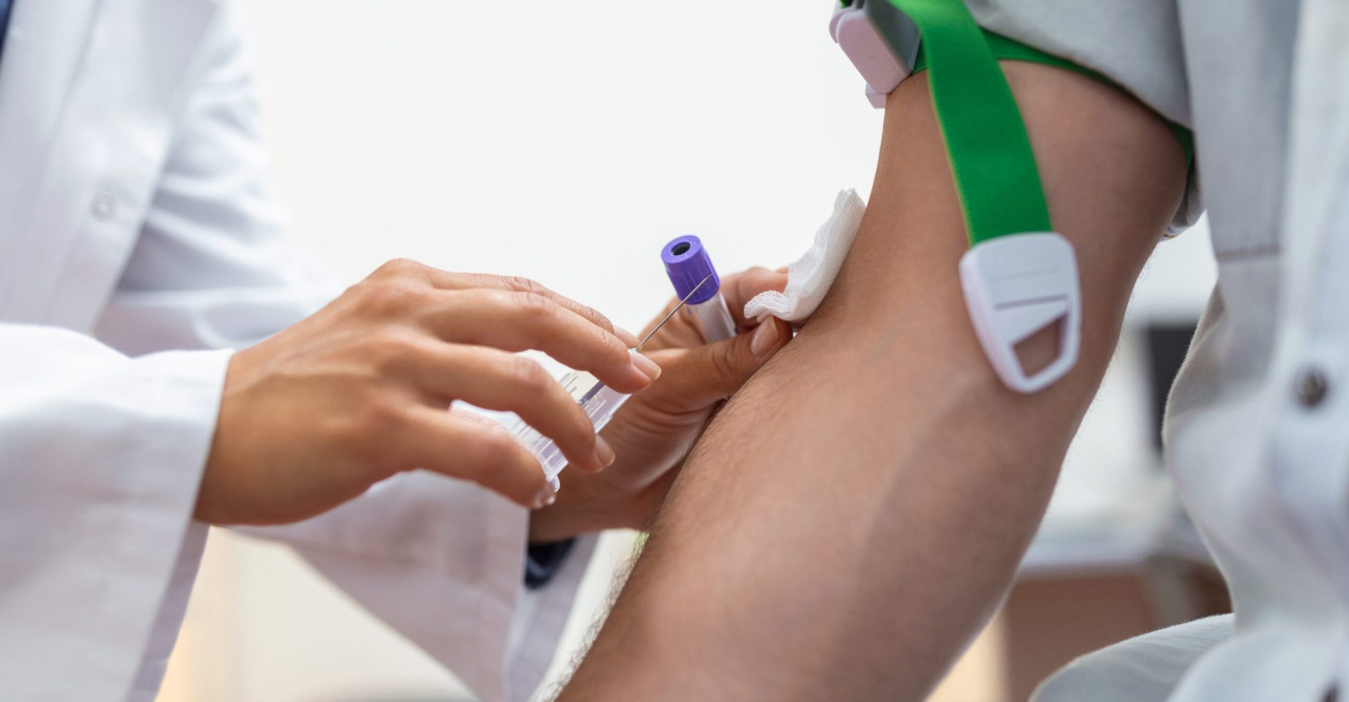 Preparation for blood test by female doctor medical uniform on the table in white bright room. Nurse pierces the patient's arm vein with needle blank tube.