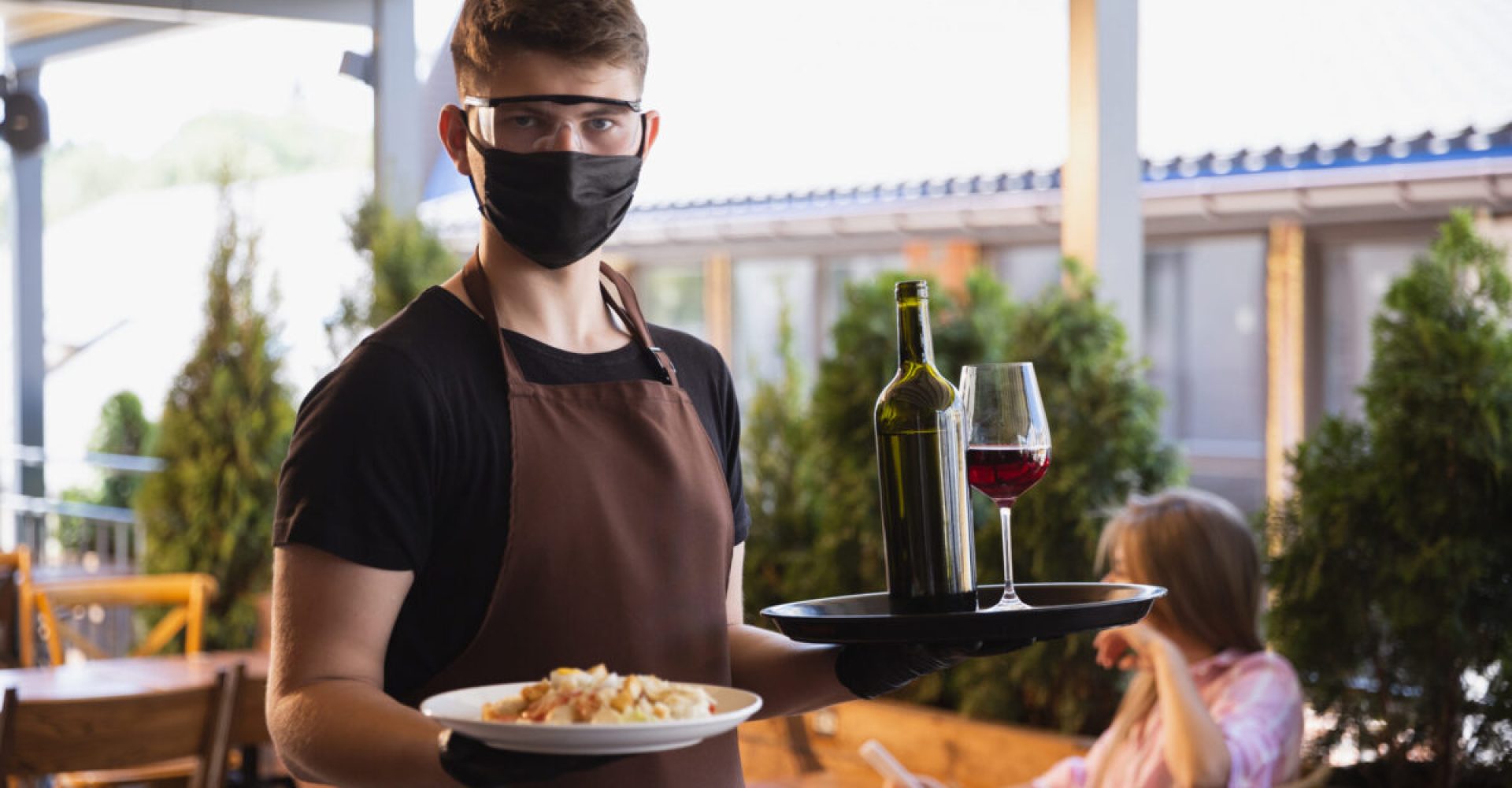 The waiter works in a restaurant in a medical mask, gloves during coronavirus pandemic