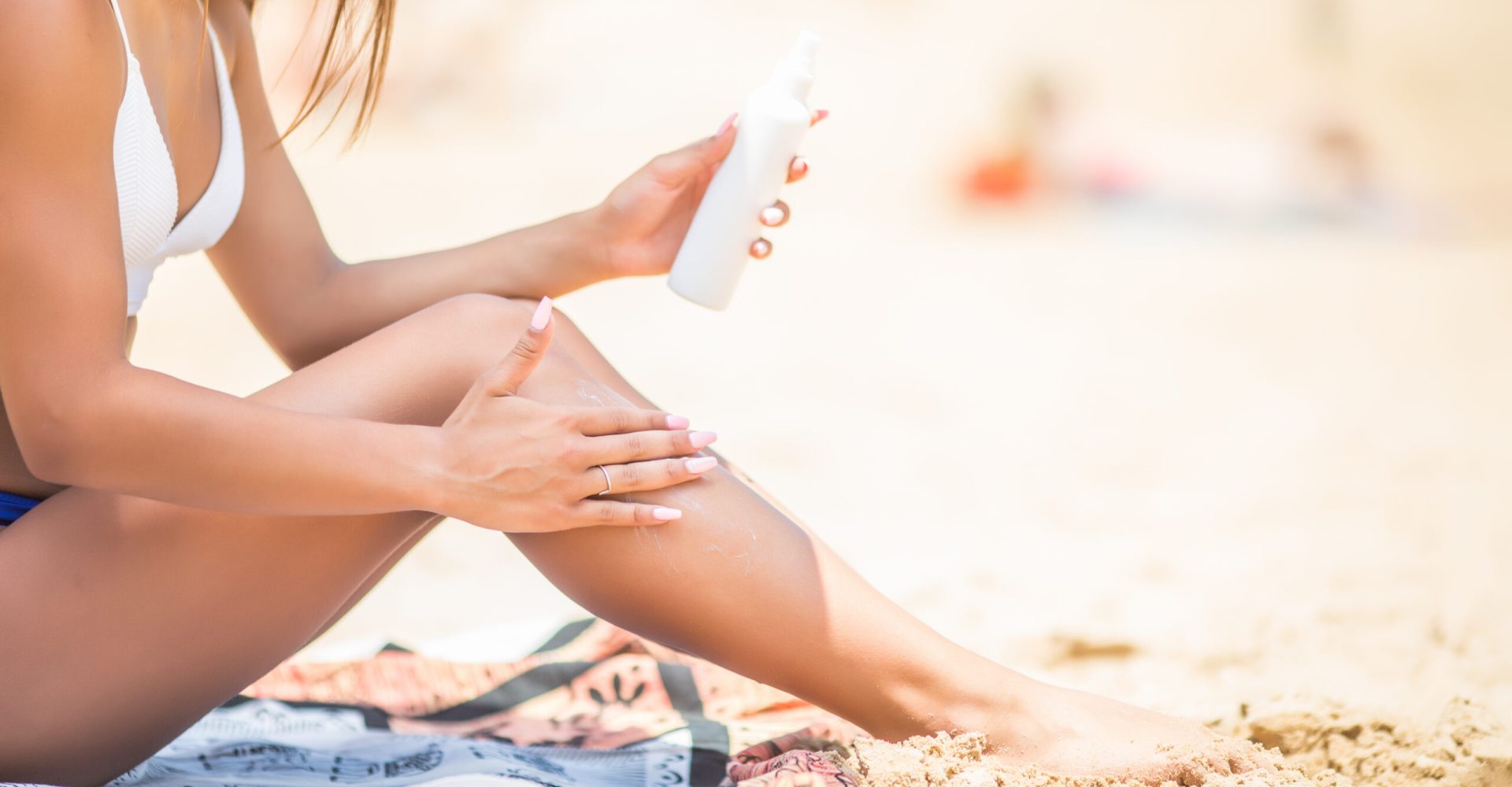 Sunscreen suntan lotion in spray bottle. Young woman in spraying tanning oil on her leg from bottle.