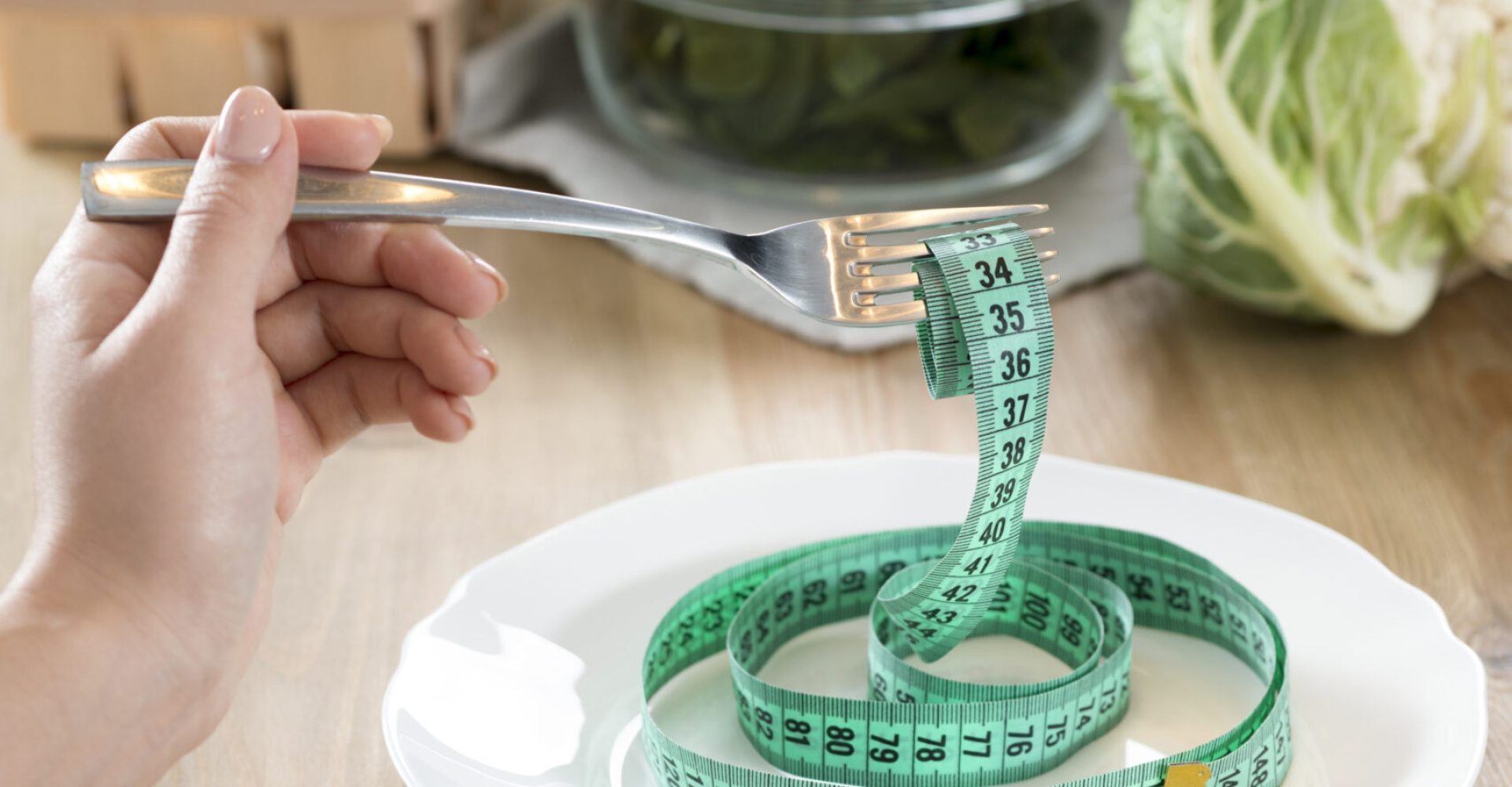 woman-s-hand-holding-fork-with-green-measurement-tape-white-plate-kitchen-counter