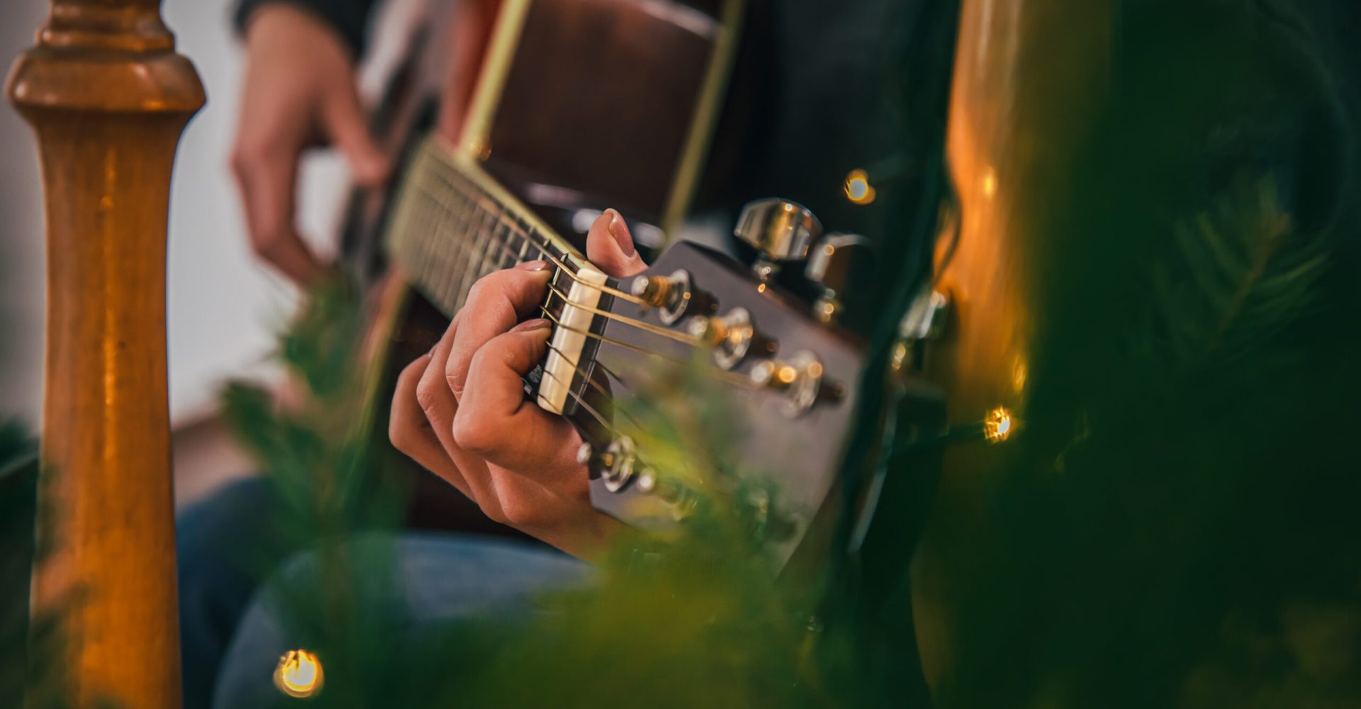 Close-up, female hands playing the guitar on a blurred background with Christmas decor.